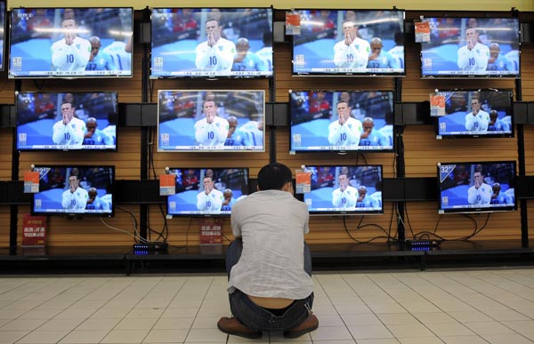 A man crouches in front of television sets broadcasting recorded footage of 2014 Brazil World Cup group match between England and Uruguay, at a home appliances store in Wuhan