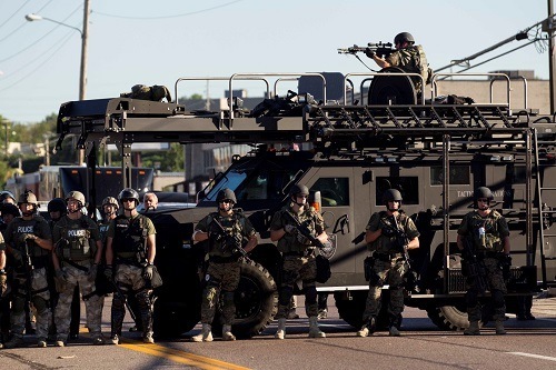 Law enforcement officers, including a sniper perched atop an armored vehicle, watch as demonstrators protest the fatal shooting of Michael Brown, in Ferguson, Mo., Aug. 13, 2014. The police chief of this St. Louis suburb said Wednesday that Brown injured the officer who later fatally shot the unarmed 18 year old ? though witnesses dispute that such an altercation occurred. (Whitney Curtis/The New York Times)