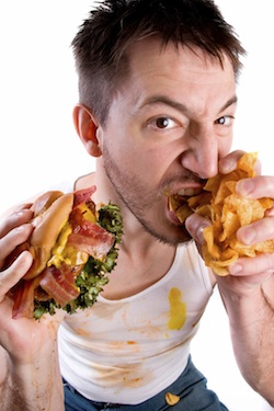 He's got his game face and game food on... messy guy cramming his face full of burger and chips.